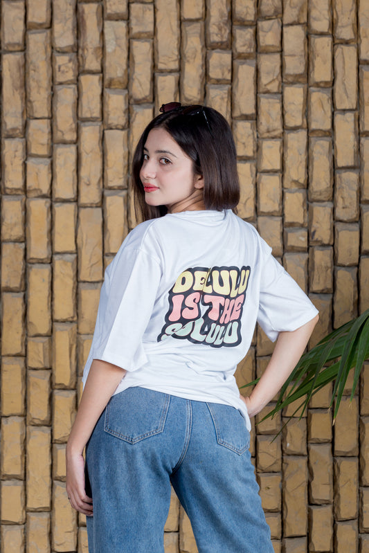 Person wearing a white t-shirt with colorful text against a brick wall.