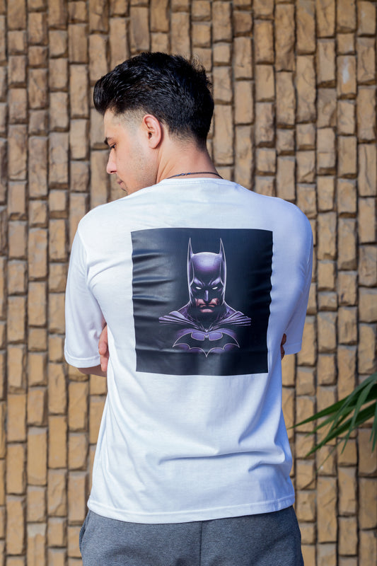 Person wearing a white t-shirt with a Batman graphic on the back against a stone wall.